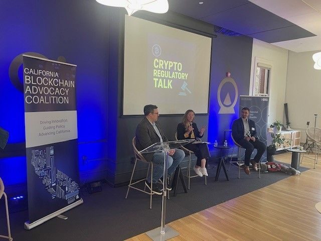 Three speakers seated on stage at the Crypto Regulatory Talk fireside chat