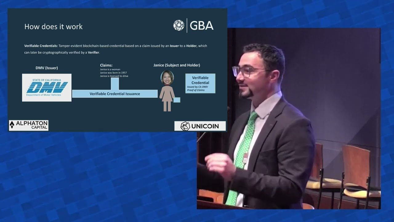 Dominic speaking at the GBA Blockchain Showcase beside a verifiable credentials slide